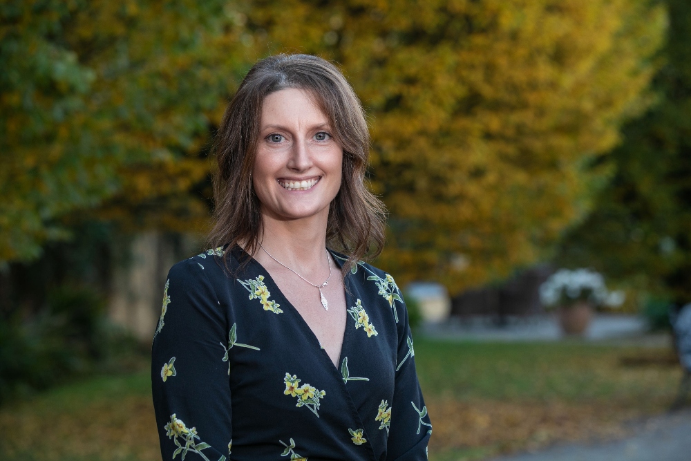 Woman in black dress standing in front of trees.